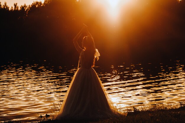 Una sposa elegante in abito bianco gode della natura al tramonto.Modella in abito da sposa nella natura nel parco.Bielorussia