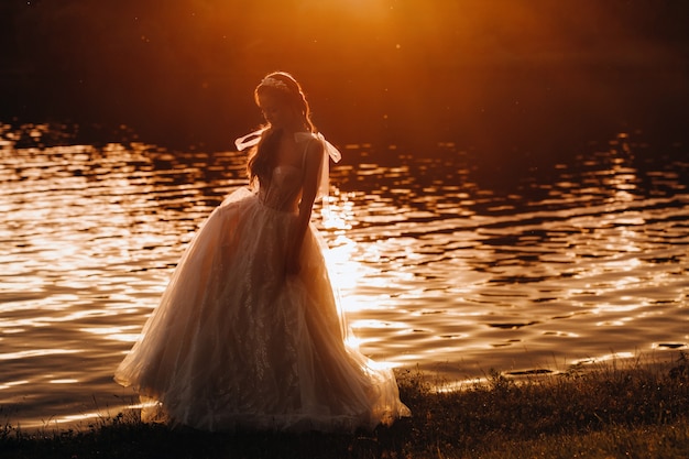 Una sposa elegante in abito bianco gode della natura al tramonto.Modella in abito da sposa nella natura nel parco.Bielorussia