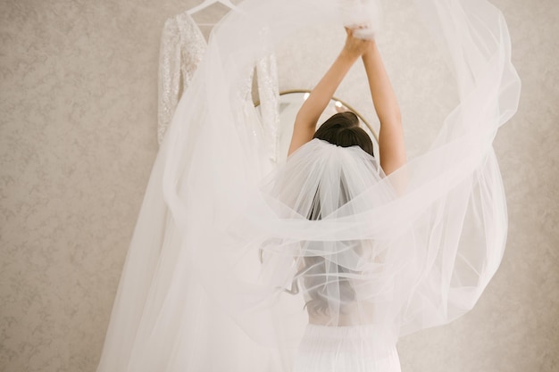 Una sposa felice balla al mattino sta in piedi con la schiena che si sviluppa un velo