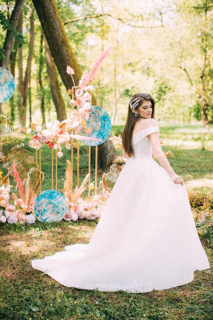 Una sposa in un tradizionale abito bianco con un bouquet da sposa accanto all'arco nuziale