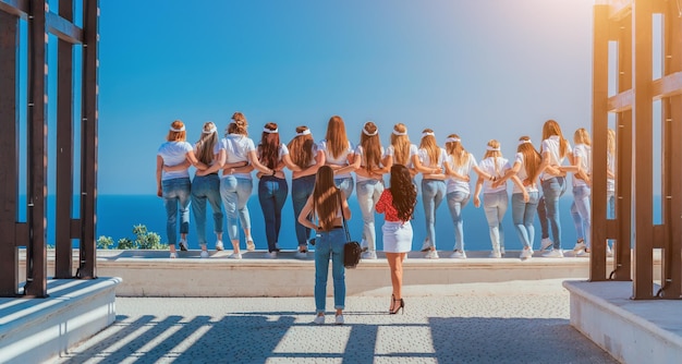 Una squadra di successo di ragazze in magliette bianche e jeans blu scatta foto abbracciandosi sul mare