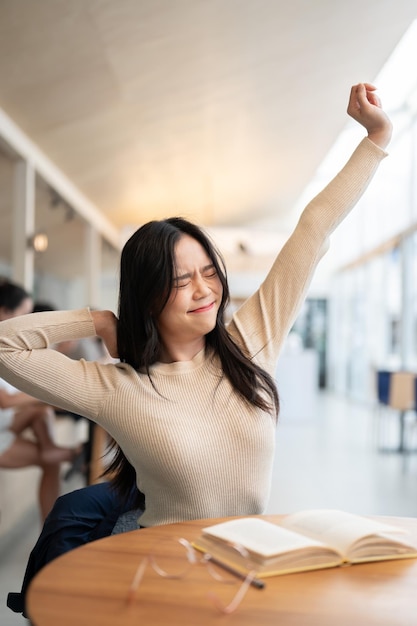 Una stanca donna asiatica allunga le braccia mentre lavora a distanza in un caffè o in una biblioteca