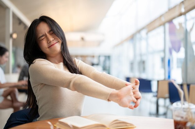 Una stanca donna asiatica allunga le braccia mentre lavora a distanza in un caffè