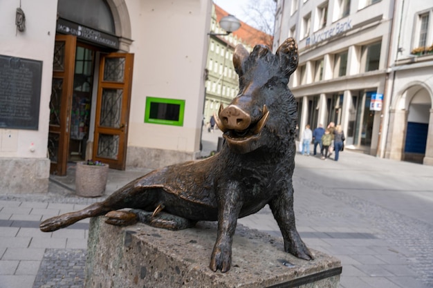 Una statua di un maiale è seduta su un piedistallo di pietra in una piazza della città
