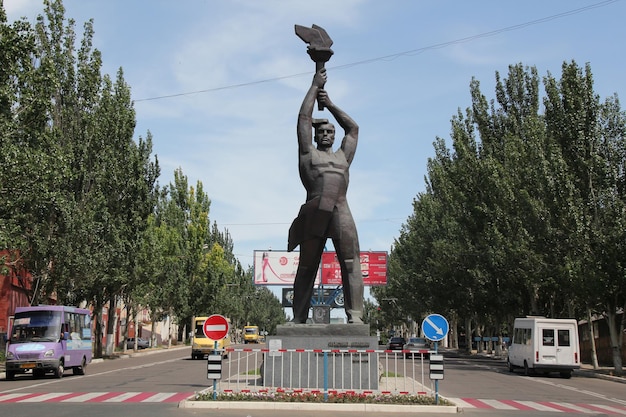 Una statua di un uomo con una bandiera in testa si trova in una strada Monumento al lavoratore di Lugansk