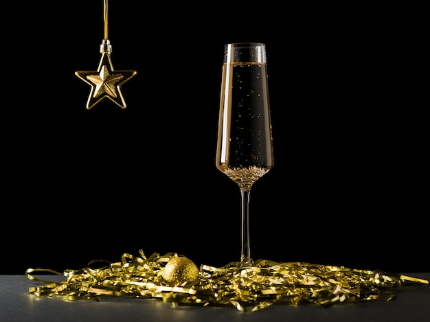 Una stella d'oro e un bicchiere di vino con un mazzo di stelle filanti sul nero.