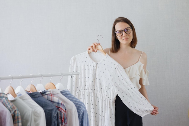 Una stilista professionista donna europea con capelli scuri e occhiali sceglie i vestiti per un'azienda