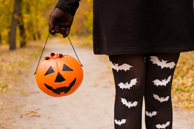 Una strega tiene un secchio di caramelle di zucca nella foresta.