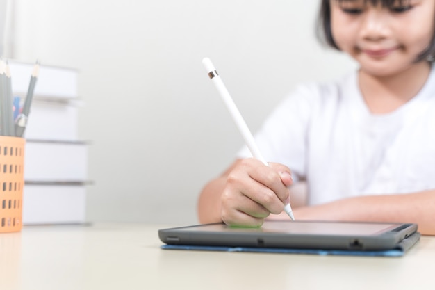 Una studentessa asiatica allegra indossa le cuffie e scrive su un tablet digitale per studiare a casa