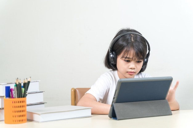 Una studentessa asiatica allegra indossa le cuffie e scrive su un tablet digitale per studiare a casa