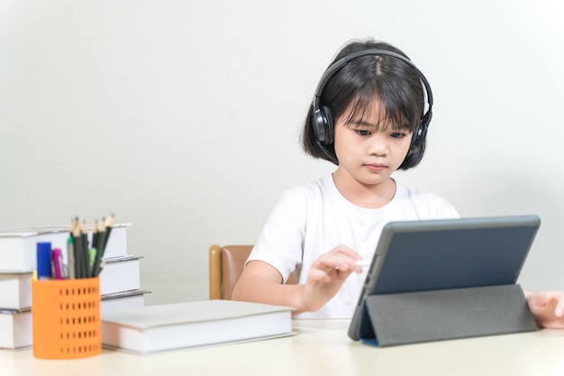 Una studentessa asiatica allegra indossa le cuffie e scrive su un tablet digitale per studiare a casa