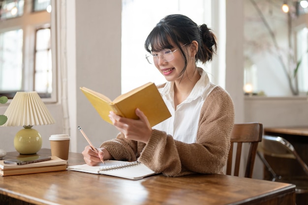 Una studentessa asiatica concentrata che fa i compiti alla ricerca di informazioni in un libro seduto a un tavolo