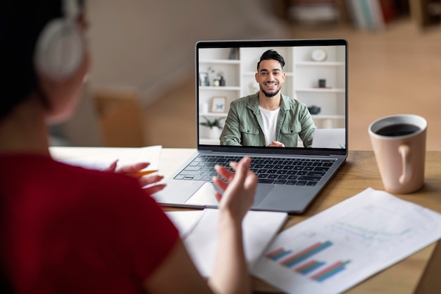 Una studentessa asiatica teenager in cuffia ha una lezione video con un insegnante arabo sullo schermo del laptop in camera