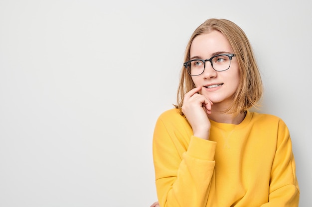 Una studentessa bionda intelligente con gli occhiali tocca il mento pensa di scegliere isolato su sfondo bianco studio con spazio per la copia Fiducia genio intelligente