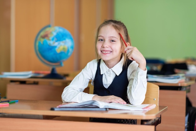 Una studentessa carina si siede a una scrivania circondata da libri Guarda nella telecamera Vita scolastica