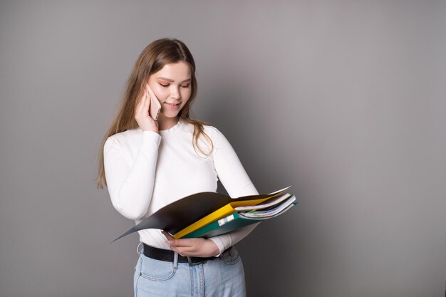 Una studentessa carina sta parlando al telefono e sta guardando una cartella aperta per i documenti