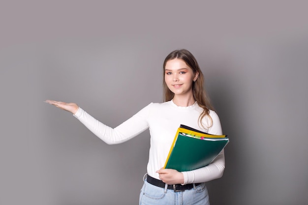 Una studentessa carina tiene dei quaderni per appunti e indica il lato con la mano