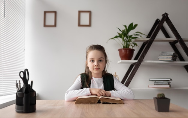 Una studentessa caucasica siede a casa a un tavolo guardando la telecamera Un libro aperto si trova sul tavolo Concetto di apprendimento online