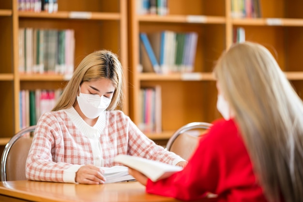 Una studentessa che indossa una maschera legge un libro nella biblioteca dell'università.