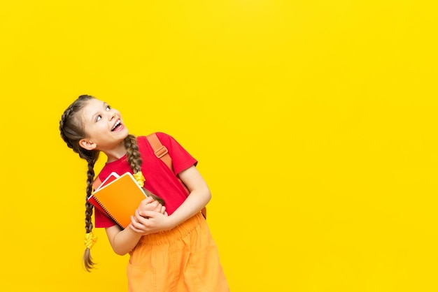 Una studentessa con una cartella guarda la tua pubblicità per corsi educativi per scolari Una bambina si sta preparando per gli esami su uno sfondo giallo isolato Copia spazio