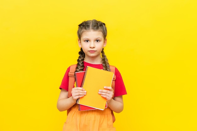Una studentessa con zaino e quaderni si sta preparando per ulteriori corsi di formazione Una bella bambina sta andando a scuola su uno sfondo giallo isolato