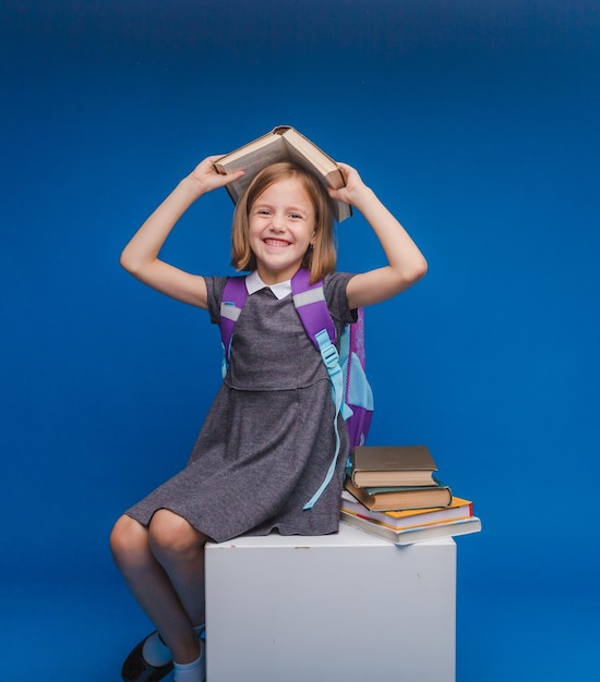 Una studentessa è seduta su un cubo bianco e sta leggendo un libro isolato su uno sfondo blu torna a scuola