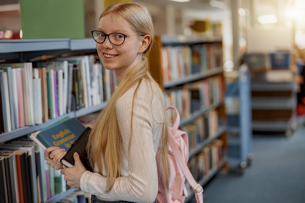 Una studentessa intelligente con gli occhiali sceglie il libro mentre si trova nella biblioteca universitaria