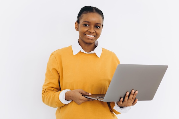 Una studentessa nera con una giacca gialla tiene un laptop su uno sfondo bianco