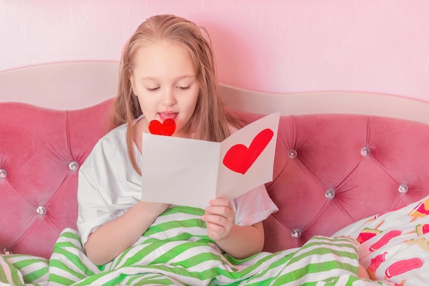 una studentessa si siede nel suo letto e legge un biglietto di auguri fatto in casa con un cuore di carta