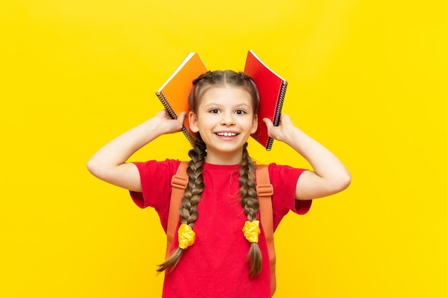 Una studentessa sta preparando una cartella per la scuola Una bambina raccoglie quaderni e libri di testo per la giornata scolastica su uno sfondo giallo isolato Preparazione per gli esami