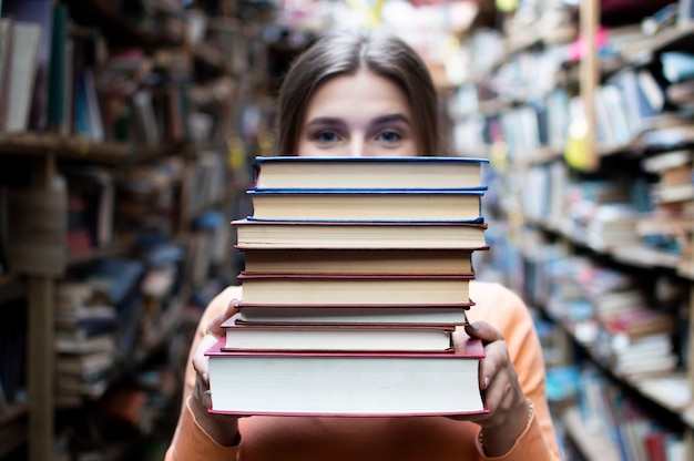 Una studentessa tiene una pila di libri in biblioteca, cerca la letteratura e si offre di leggere, una donna si prepara per lo studio, la conoscenza è potere, il libraio in libreria