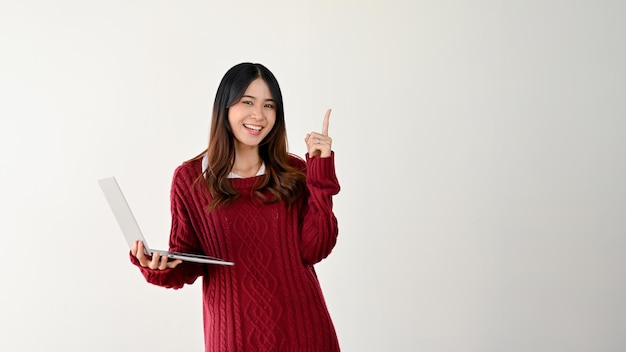 Una studentessa universitaria asiatica sorridente sta puntando il dito verso l'alto e tenendo in mano il suo computer portatile