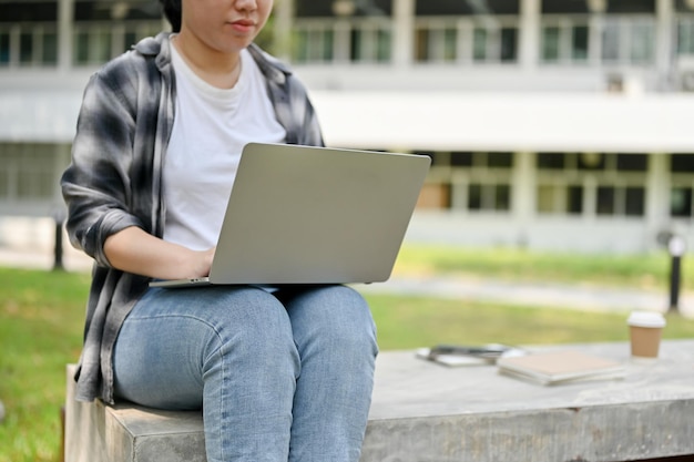 Una studentessa universitaria che utilizza il suo laptop portatile su una panchina in un parco del campus