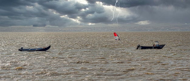 Una tavola da windsurf che naviga sul fiume Tago in un giorno di temporale con Lisbona sullo sfondo