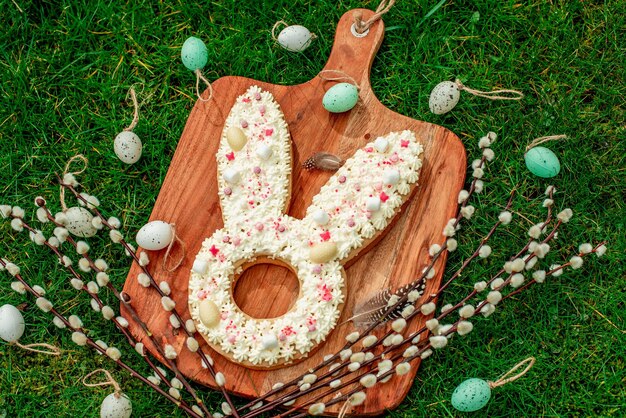 Una tavola di legno con un biscotto a forma di coniglietto fatto con uova di pasqua di cioccolato bianco e decorato con uova di pasqua.