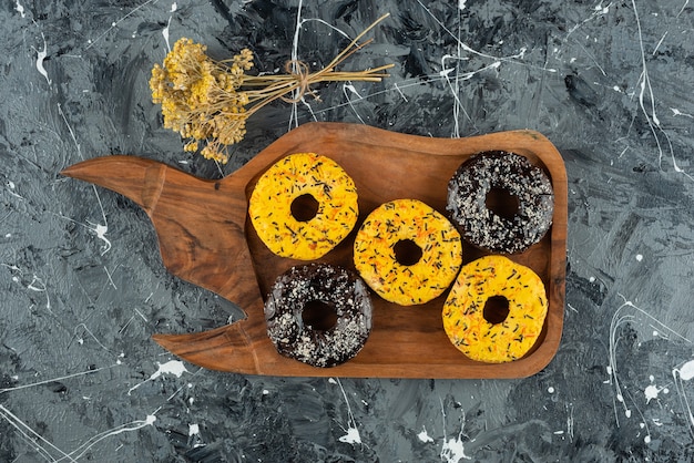 Una tavola di legno di ciambelle glassate fresche gialle e cioccolato.