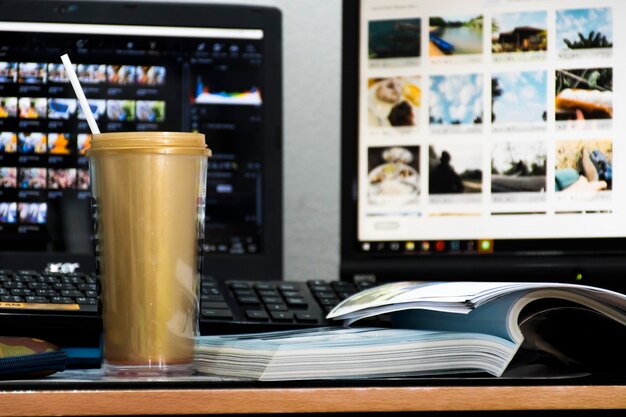 Una tazza d'oro si trova sul tavolo e un libro è posto accanto ad essa. E con lo sfondo, c'è un notebook e il monitor di un computer.