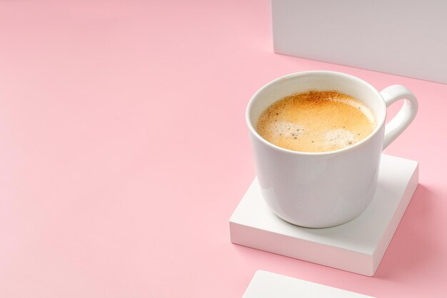 Una tazza da caffè con cappuccino su podio quadrato bianco e sfondo rosa Bevanda espresso sul podio