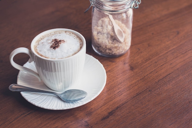 Una tazza del caffè del cappuccino con la bottiglia dello zucchero sul fondo di legno della tavola con il filtro d&#39;annata