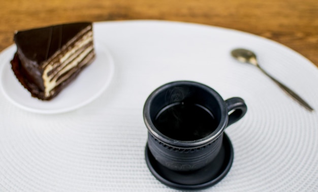 Una tazza di argilla nera con caffè e una torta su un piatto bianco