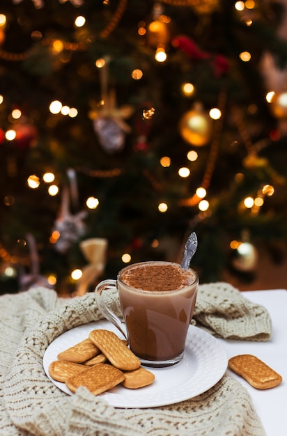 Una tazza di cacao e biscotti su un piatto bianco sul tavolo di un albero di Natale, comfort domestico