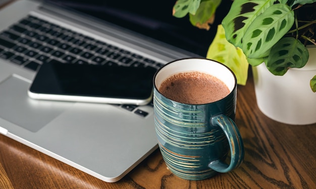 Una tazza di cacao uno smartphone un vaso di fiori e un laptop sul desktop