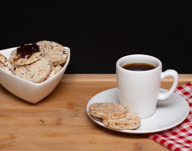 Una tazza di caffè accanto a biscotti vegani di riso con gelatina sulla parte superiore e una ciotola piena di biscotti di riso