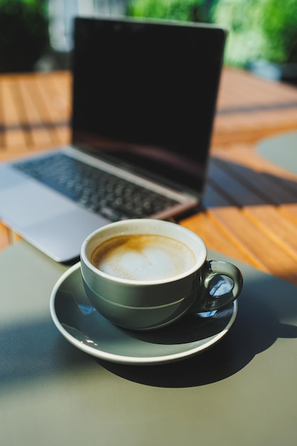 Una tazza di caffè aromatico sullo sfondo di un portatile su una terrazza estiva Lavoro in un caffè Lavoro remoto online