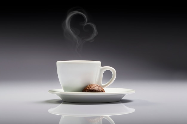 Una tazza di caffè bianco con un biscotto marrone e fumo a forma di cuore in uno sfondo neutro