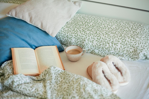 Una tazza di caffè caldo libro pantofole morbide sul letto colazione a letto casa accogliente.