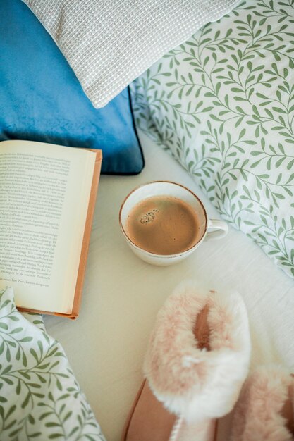 Una tazza di caffè caldo libro pantofole morbide sul letto colazione a letto casa accogliente.