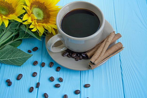 Una tazza di caffè, chicchi di caffè, cannella e girasole su sfondo blu. Mood estivo.