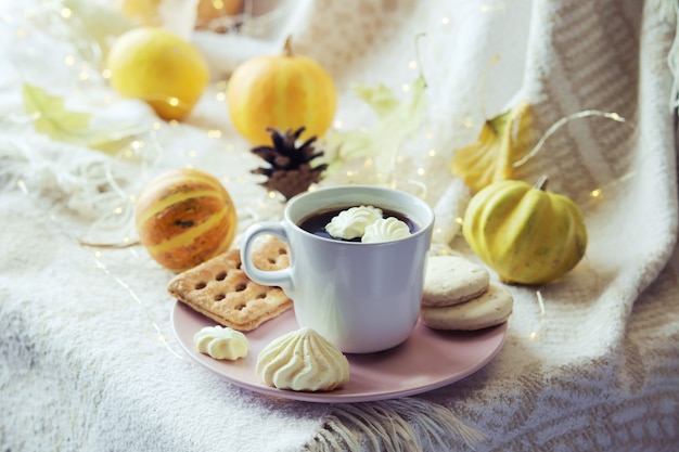 Una tazza di caffè con biscotti di meringa e zucche lascia su un caldo plaid che illumina il concetto di comfort domestico