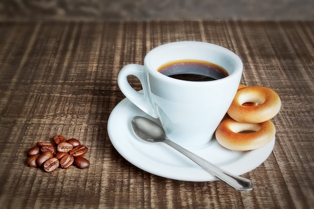 Una tazza di caffè con cracknel al forno, bagel. Chicchi di caffè sul tavolo di legno